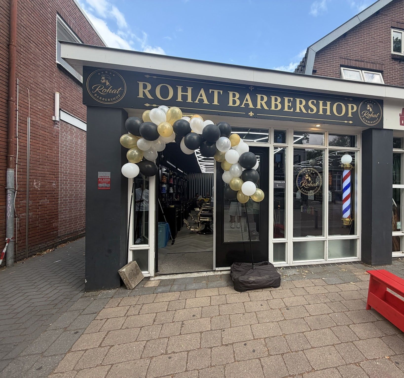 De gevel van Rohat Barbershop met gouden letters, een barberpaal en een ballonnenboog van de opening