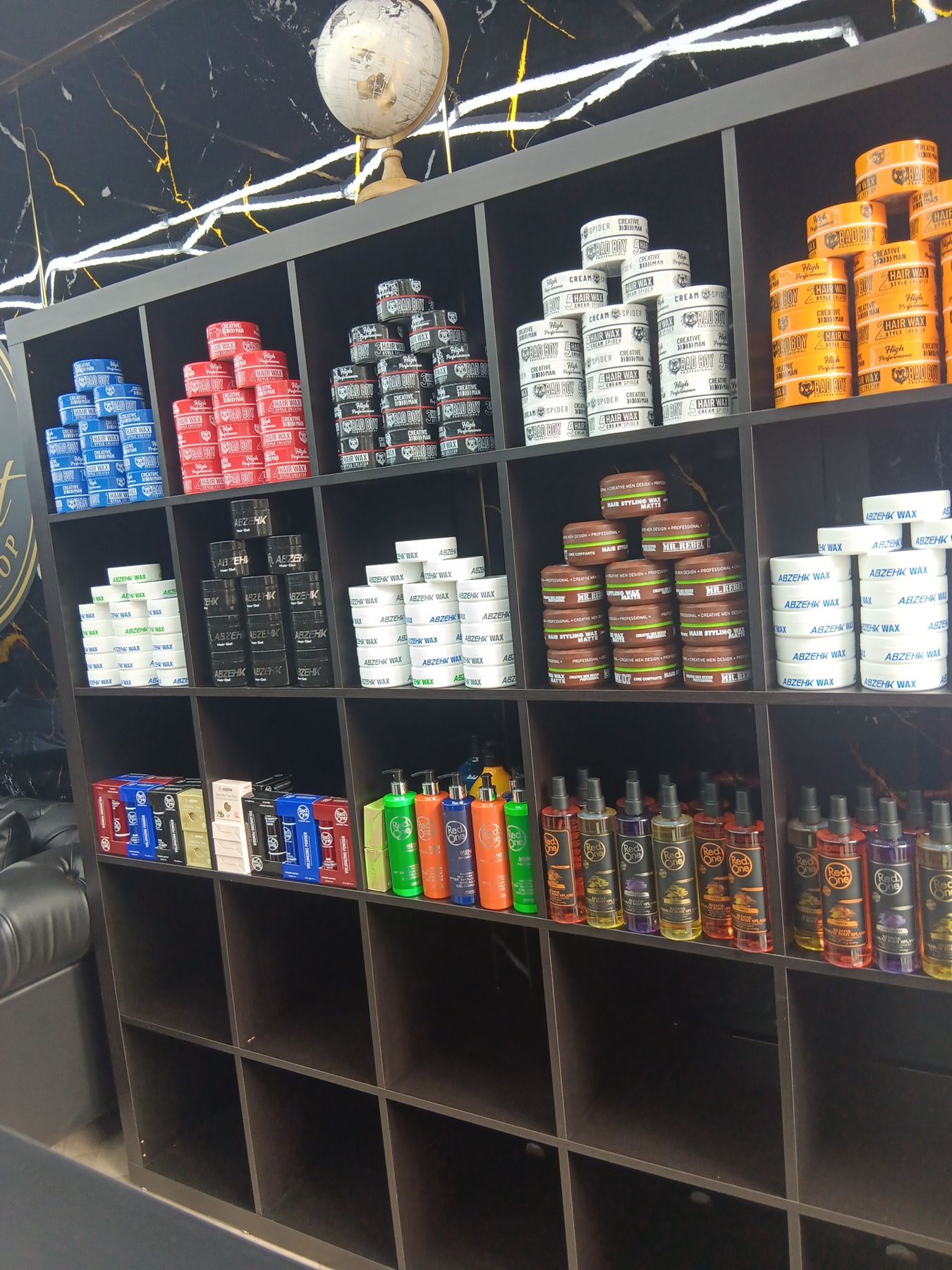 Wand met stylingproducten: wax, cream en sprays in rijen op zwarte schappen