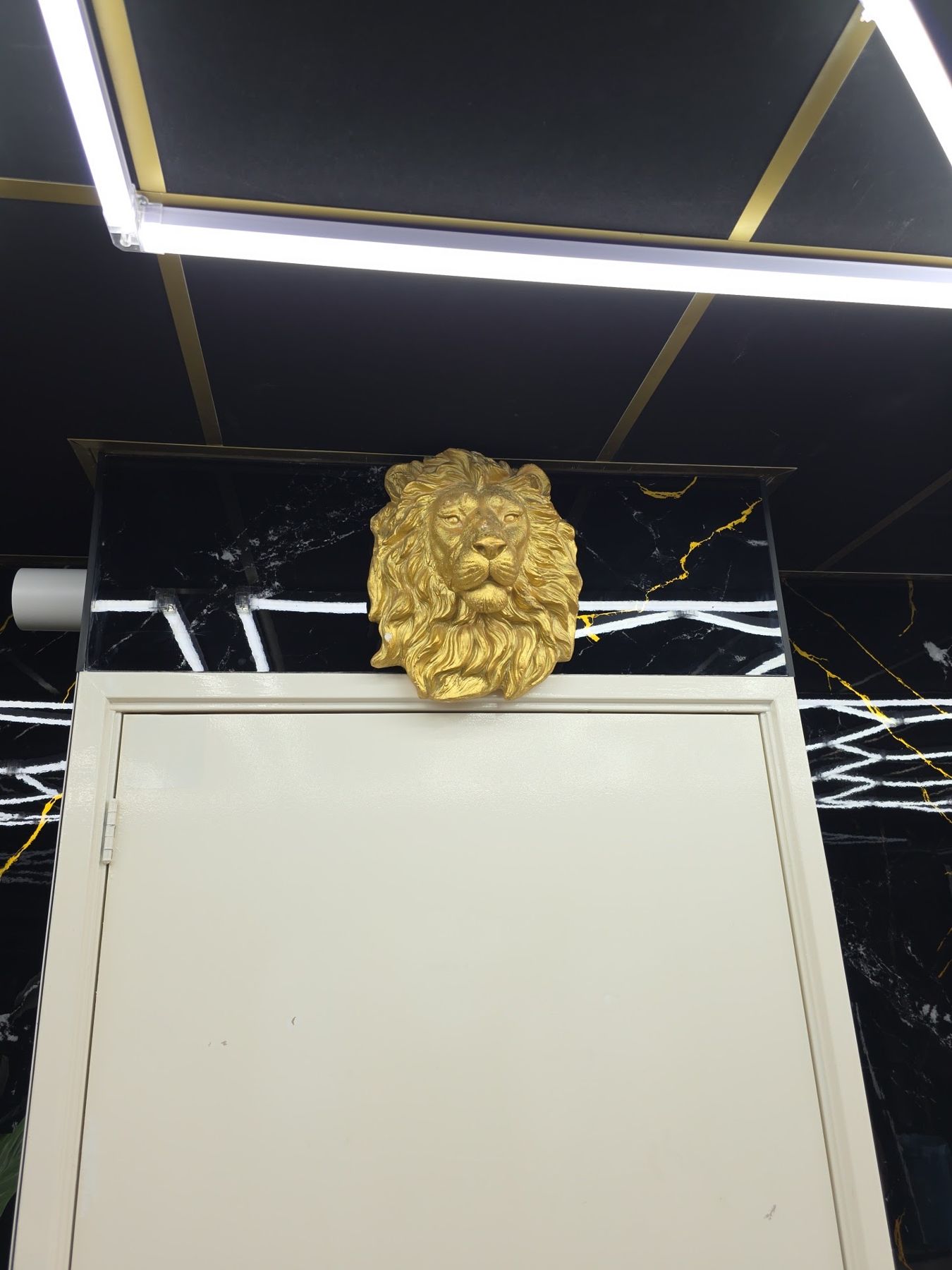 Gouden leeuwenkop boven een deur, tegen een zwarte marmeren wand met gouden aders